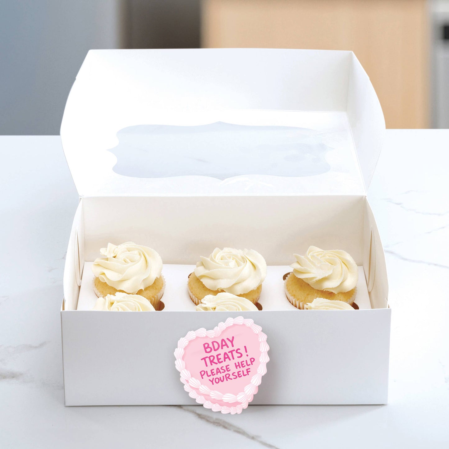 Box of cupcakes with a pink label on a marble surface