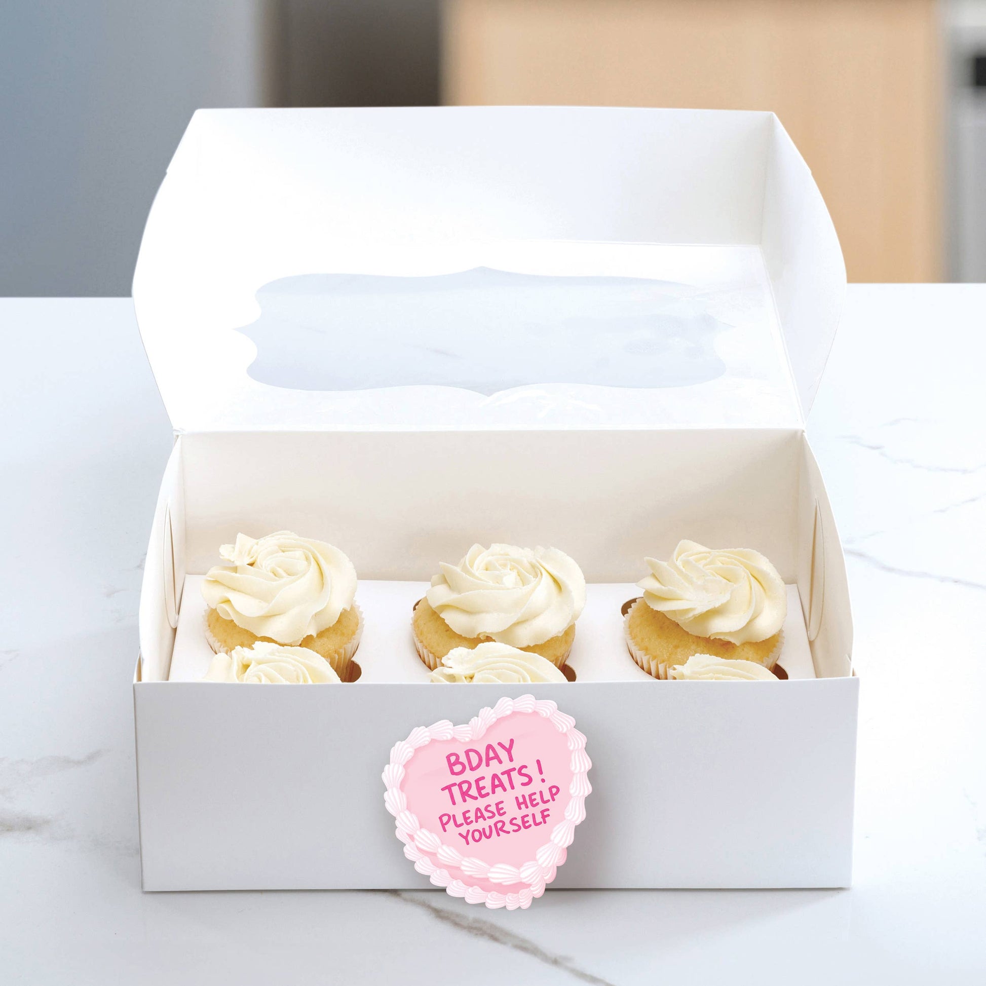 Box of cupcakes with a pink label on a marble surface