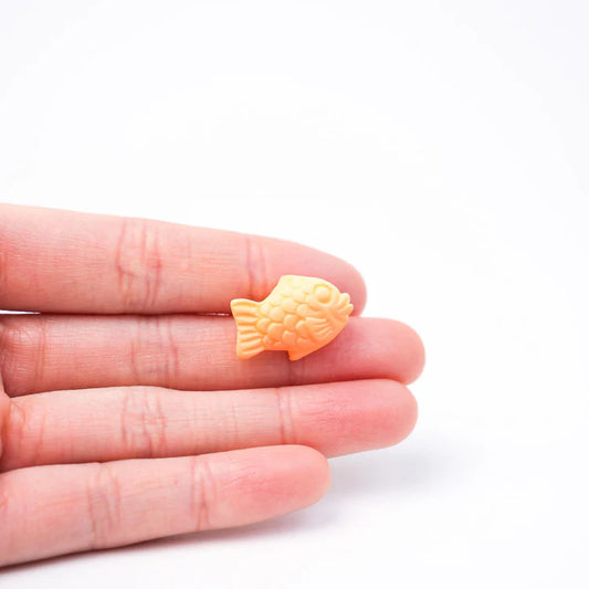 Small orange fish-shaped object held between fingers on a white background