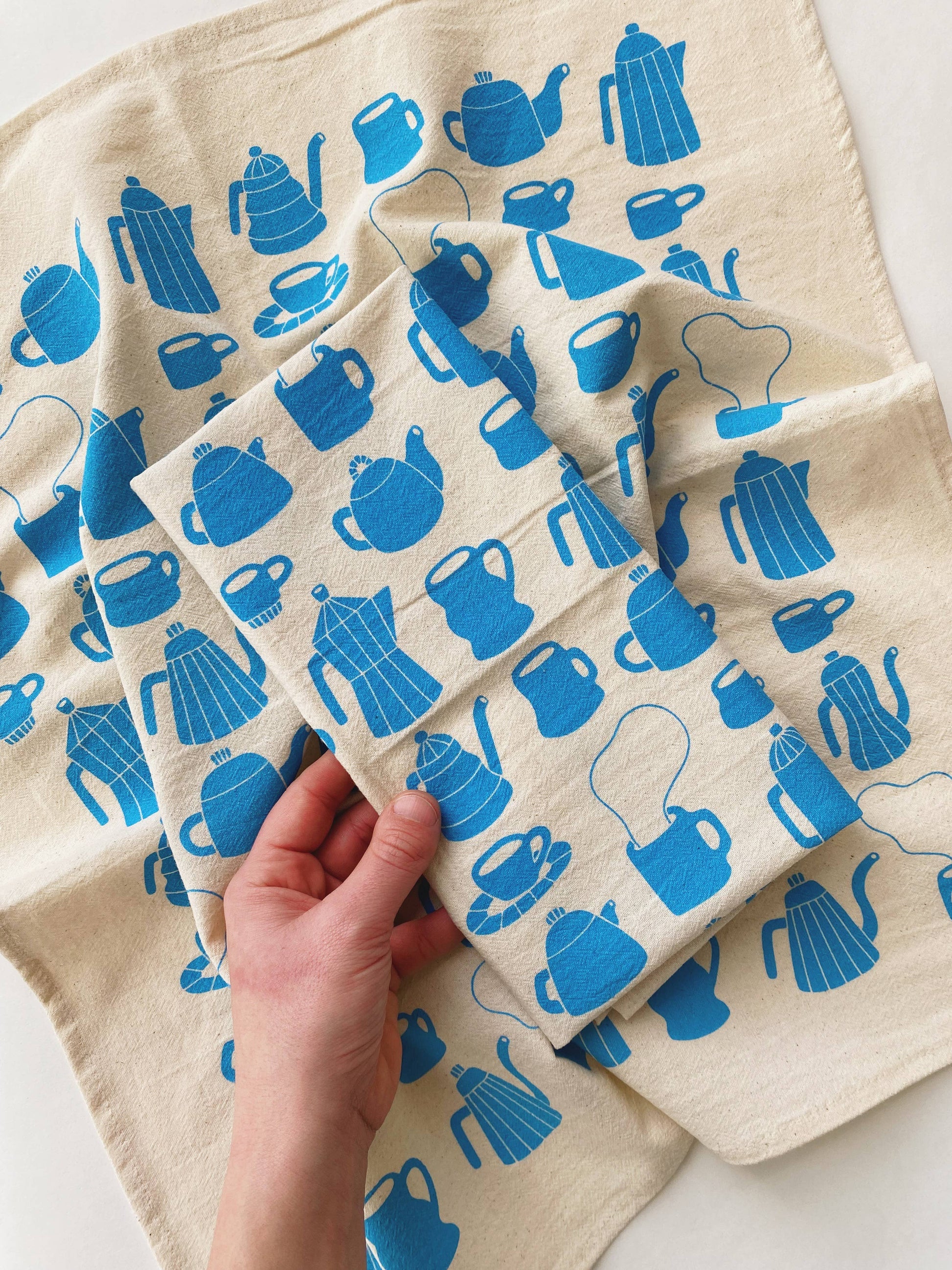 Tea towel with different styles of tea/coffee pots and mugs printed in blue ink on it