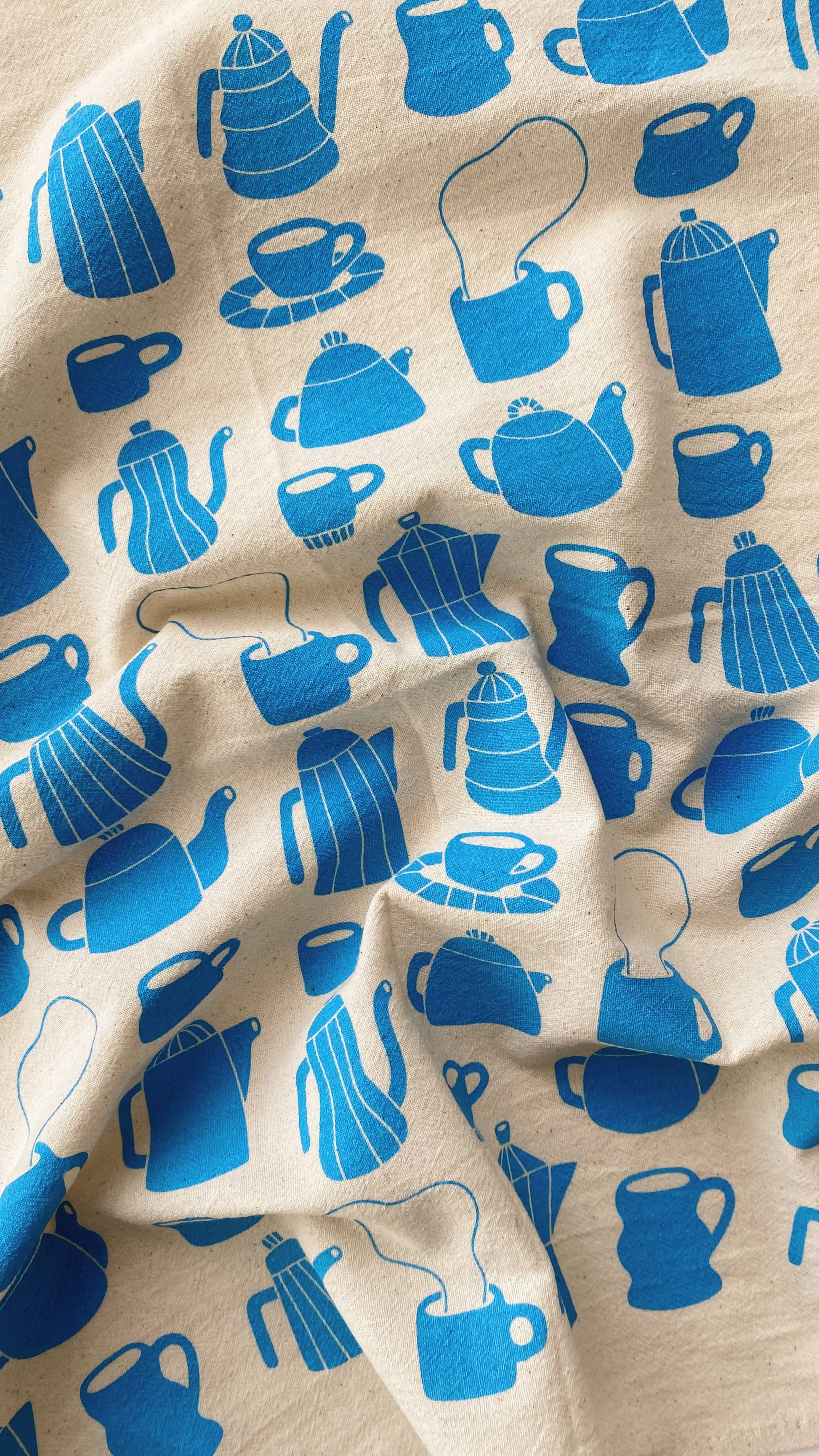 Tea towel with different styles of tea/coffee pots and mugs printed in blue ink on it