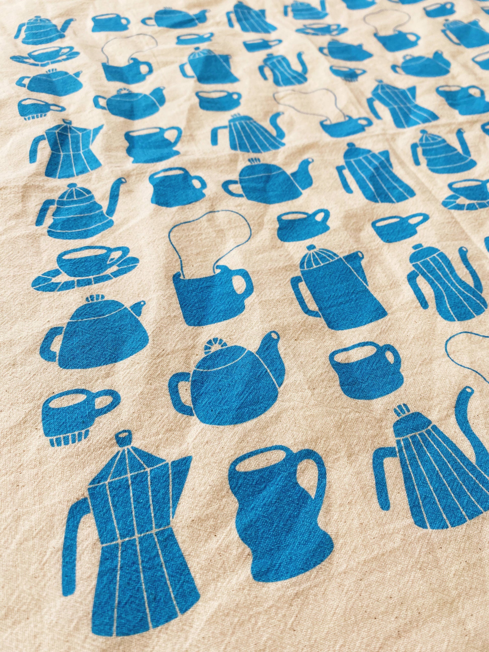 Tea towel with different styles of tea/coffee pots and mugs printed in blue ink on it