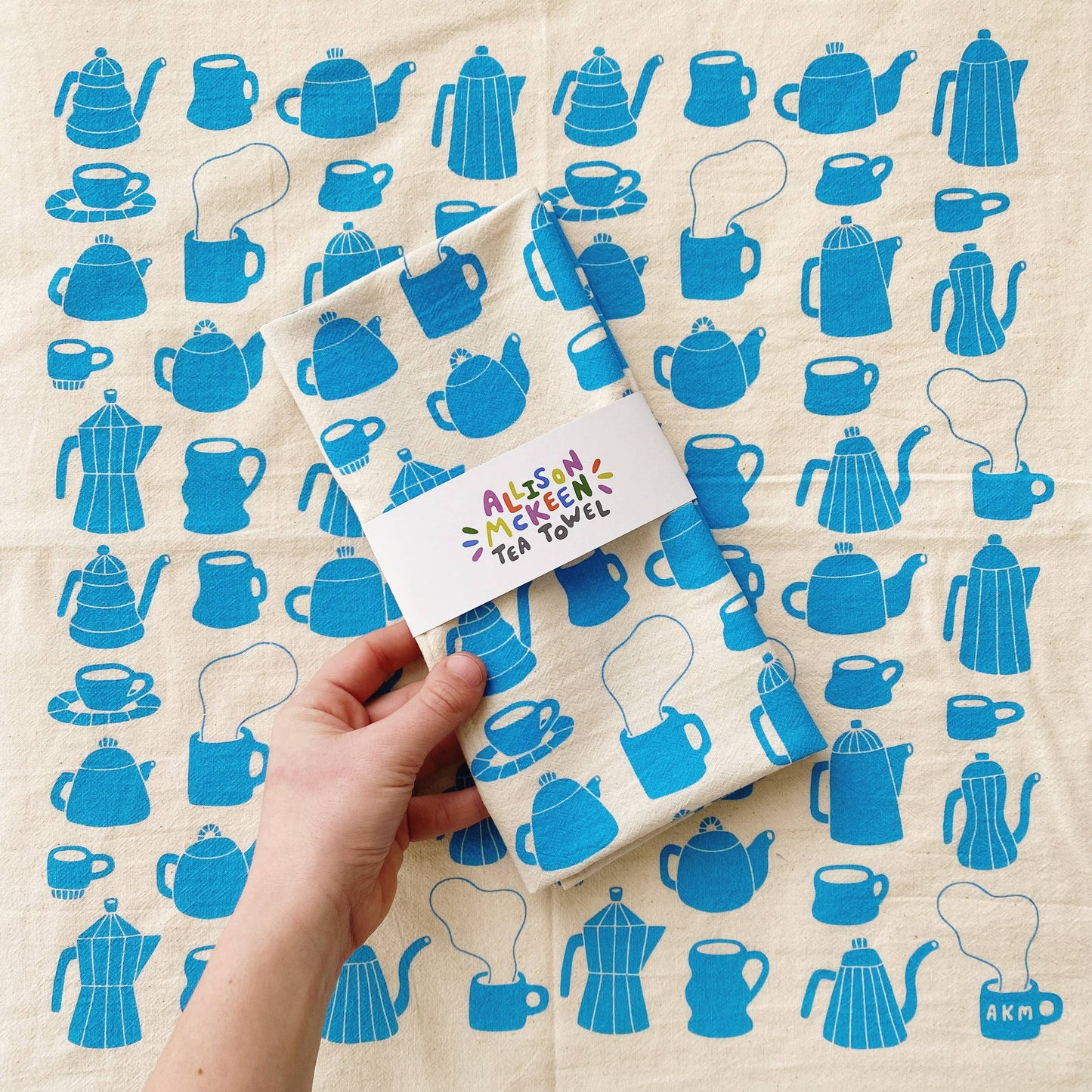 Tea towel with different styles of tea/coffee pots and mugs printed in blue ink on it