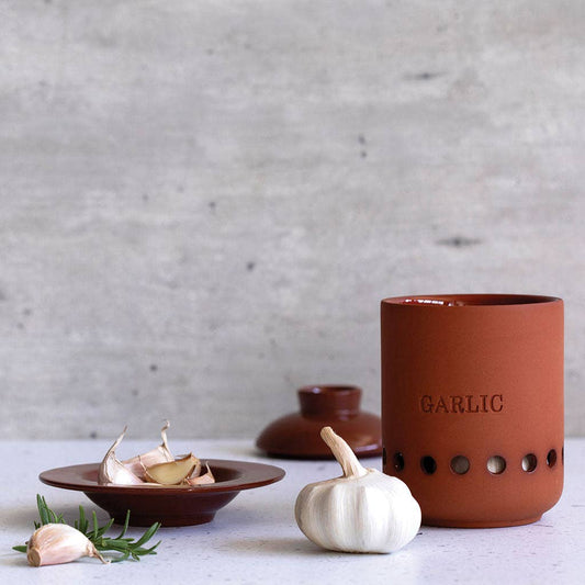 Terracotta garlic keeper with a garlic bulb on a light surface.
