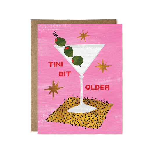 Greeting card with a martini glass and  three olives on a pink background. Text reads "Tini bit older" 