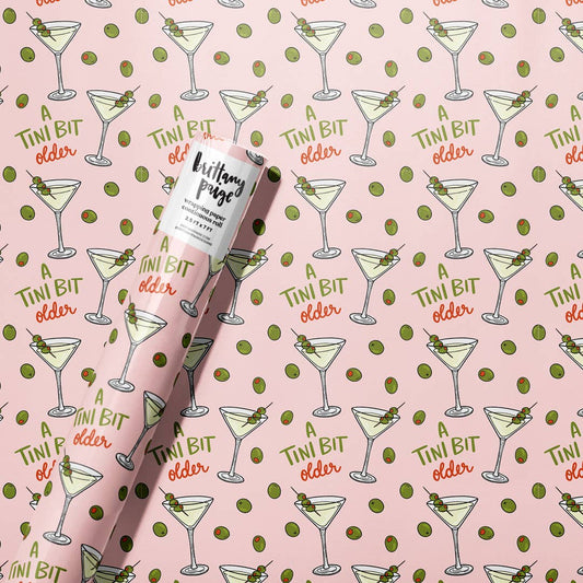 Roll of wrapping paper featuring a dirty olive martini and single olive illustration design all over, along with text that reads "A tini bit older" 