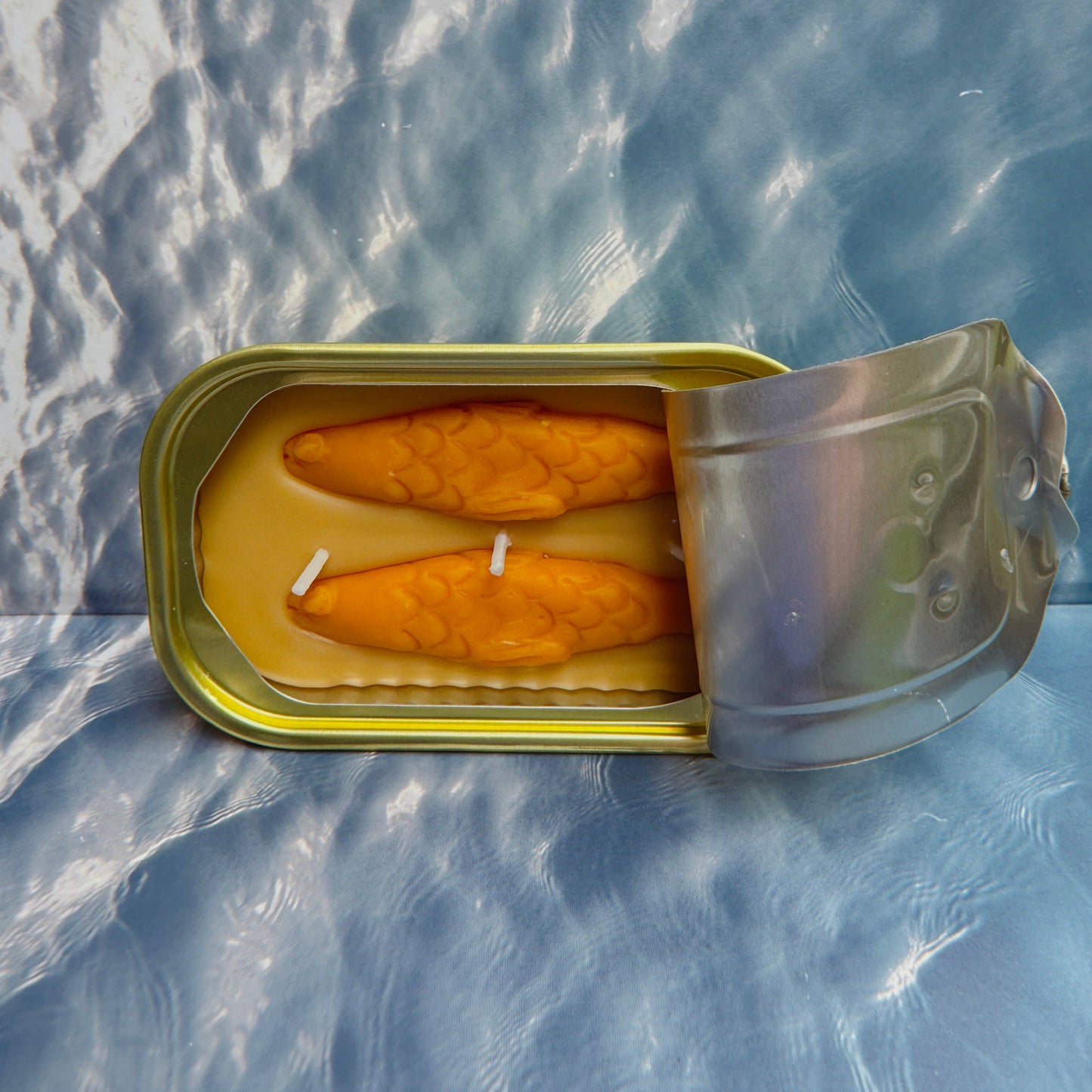 Open can of tinned fish candle on a textured blue background