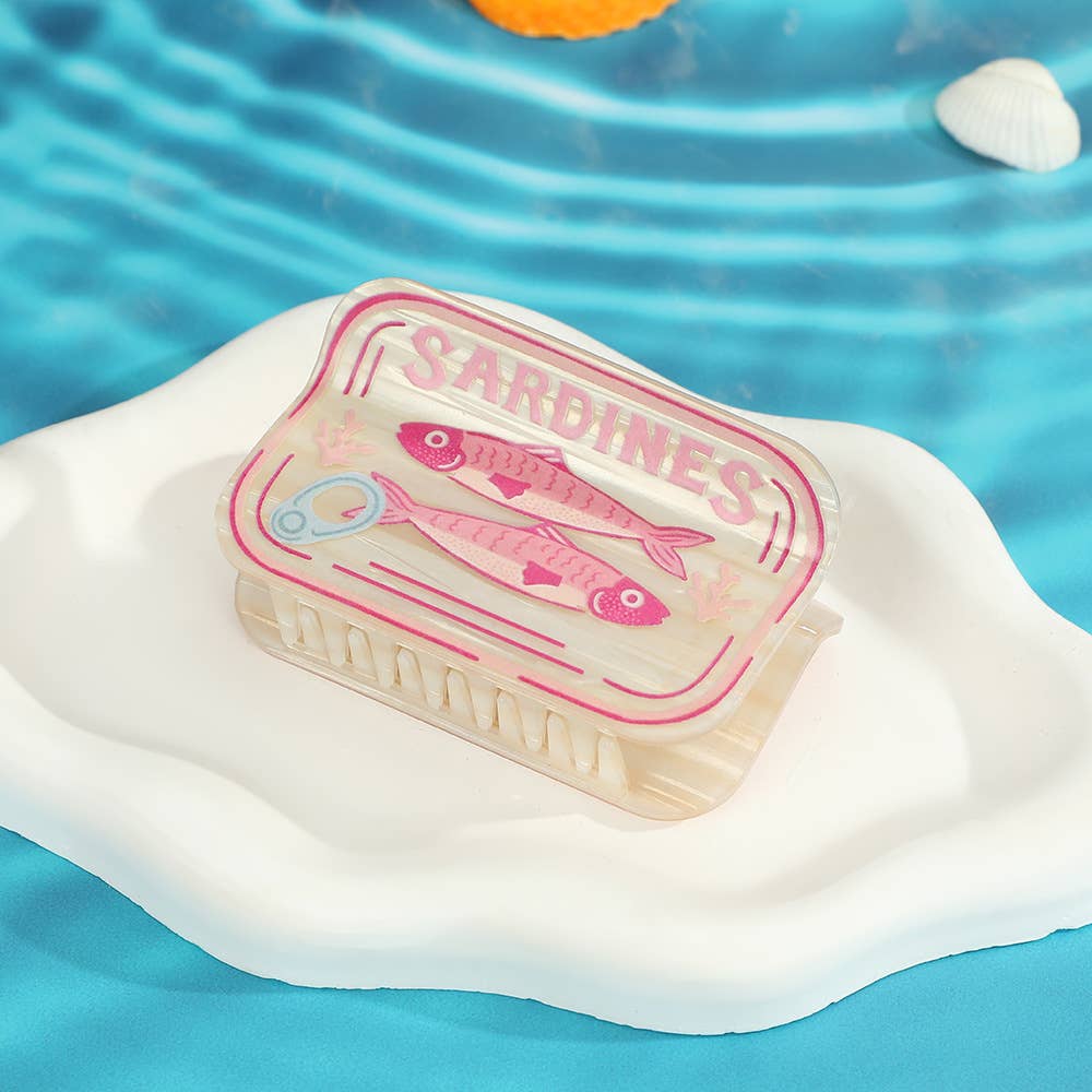White sardine can-shaped hair claw on a white surface with a blue water background