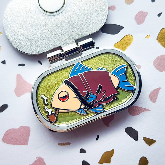 Alaskan Smoked Salmon container as an enamel pin, when opened it features a fish design smoking a pipe on a colorful background
