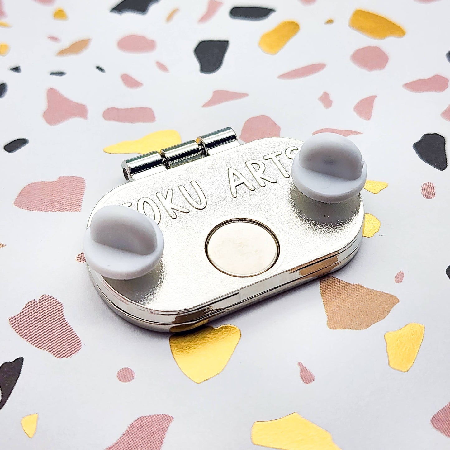 Back of the tinned smoked salmon enamel pin, showcasing the brand design and two rubber backings 