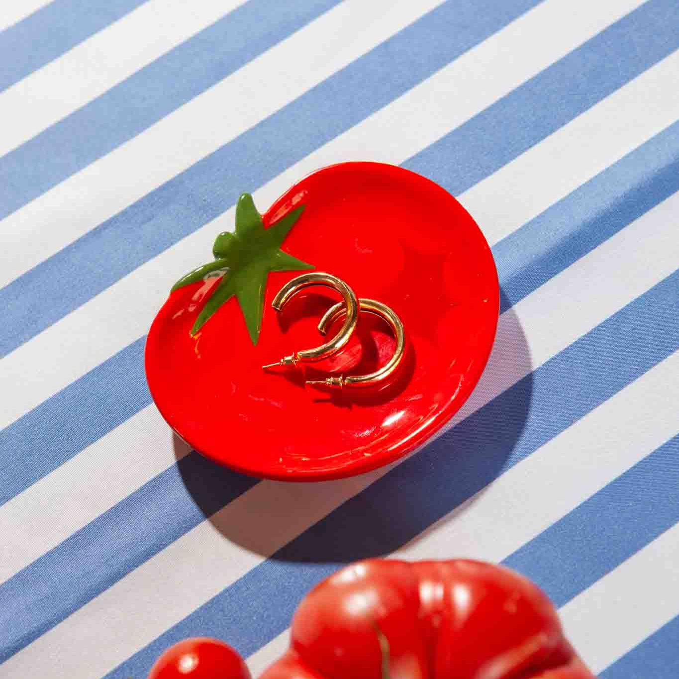 Red ceramic tomato-shaped dish with gold rings on a blue and white striped background