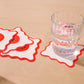 Coasters with tomato design on a beige surface with a glass of water.
