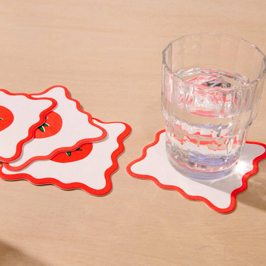 Coasters with tomato design on a beige surface with a glass of water.