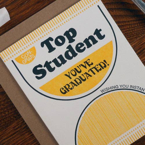 Graduation card with 'Top Student You've Graduated!' text on a wooden surface