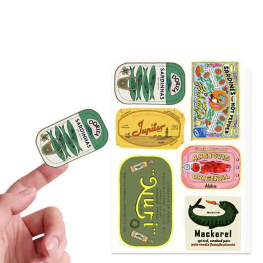 Collection of vintage-style canned fish labels held by a hand on a white background