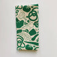 Kitchen towel with various veggies on it including, tomatoes, garlic, mushrooms, bell pepper, beets. Printed with green ink on natural colored towel 