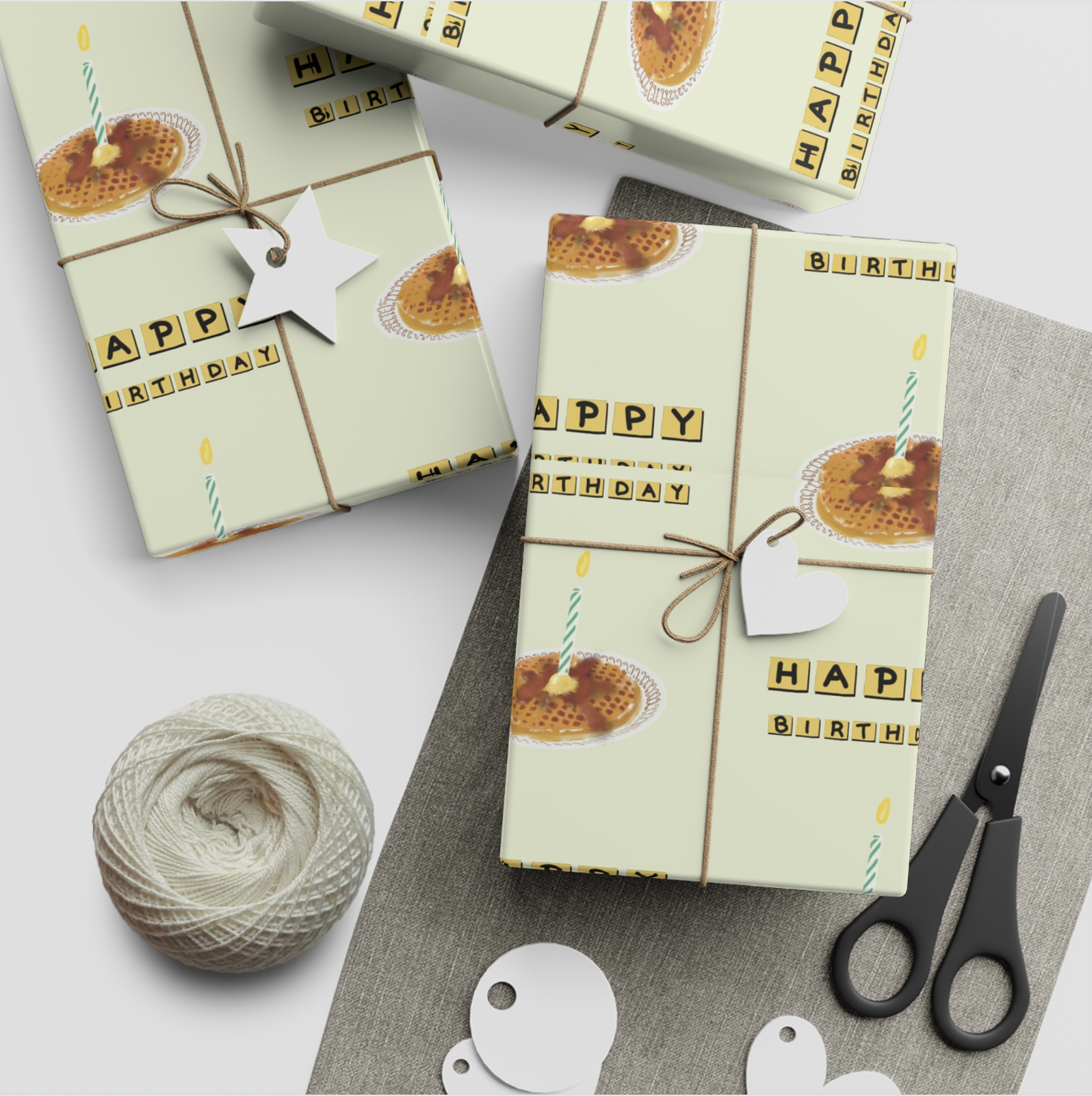 Gift boxes with 'Happy Birthday' wrapping paper, scissors, and yarn on a white surface.