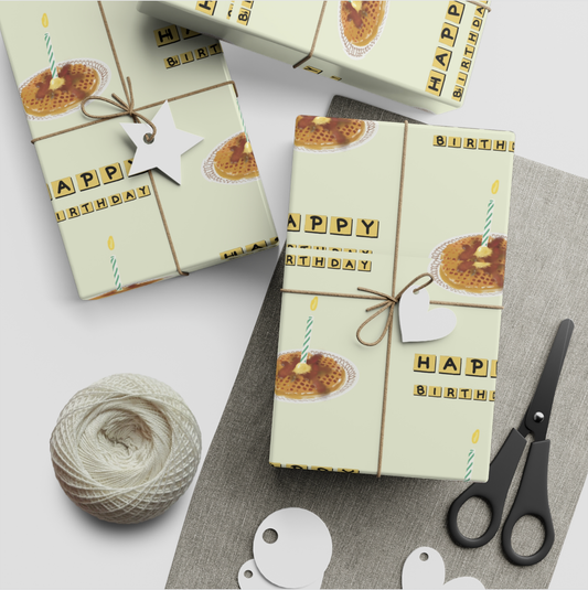 Gift boxes with 'Happy Birthday' wrapping paper, scissors, and yarn on a white surface.