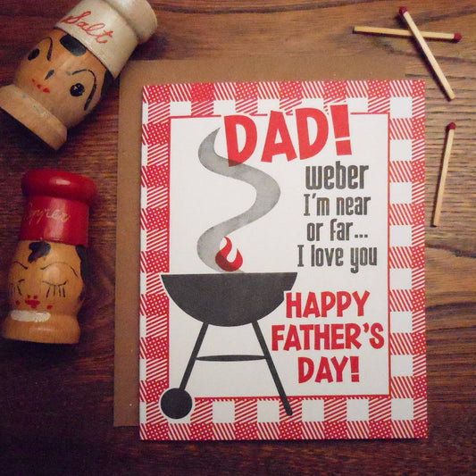 Father's Day card with BBQ graphic and text on a wooden surface with matchsticks and salt and pepper shakers.