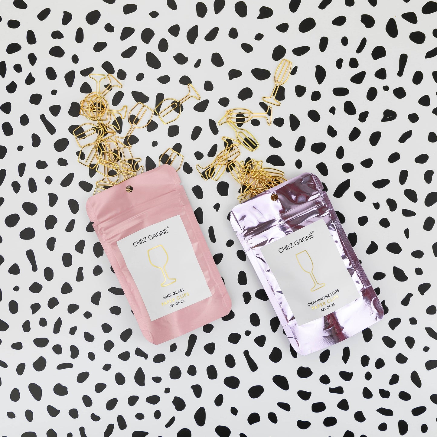 Two small packages of Chez Gagne wine and champagne glass shaped paper clips on a black and white patterned background 