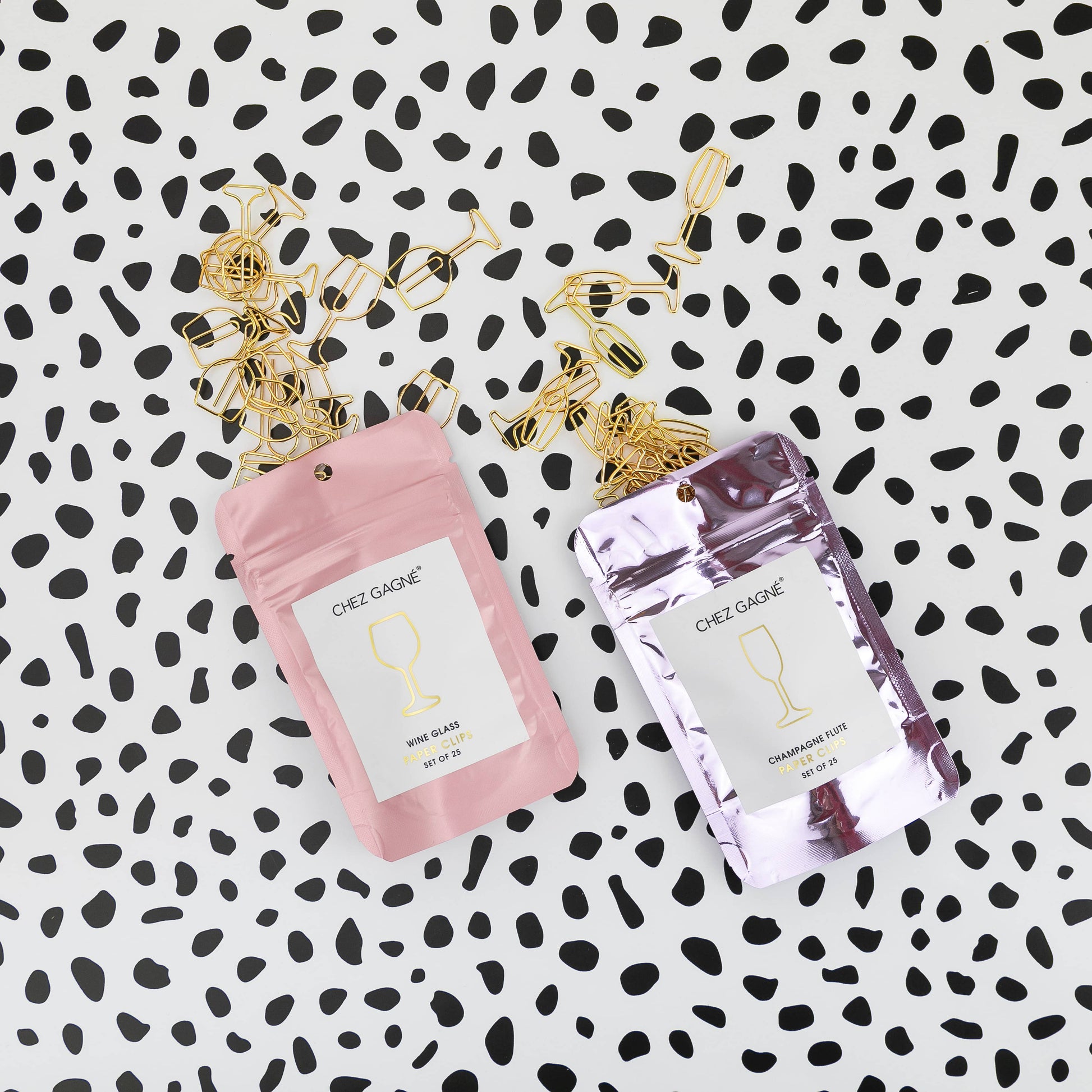 Two small packages of Chez Gagne wine and champagne glass shaped paper clips on a black and white patterned background 