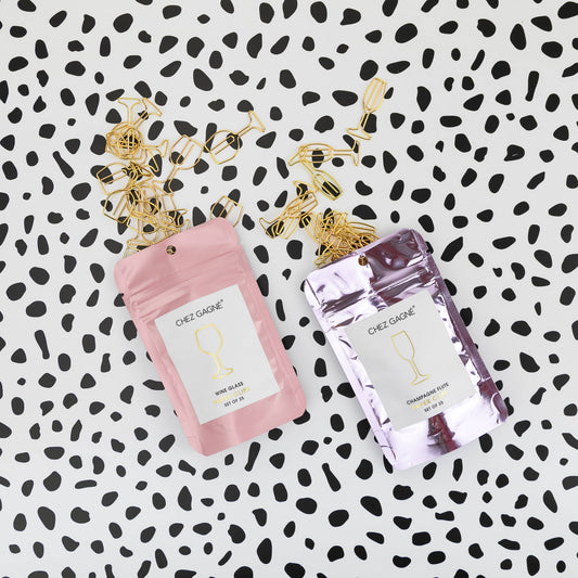 Two small packages of Chez Gagne wine and champagne glass shaped paper clips on a black and white patterned background 