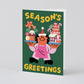 holiday greeting card that reads "season's greetings" Has illustration of a man wearing a santa hat holding two trays of holiday treats