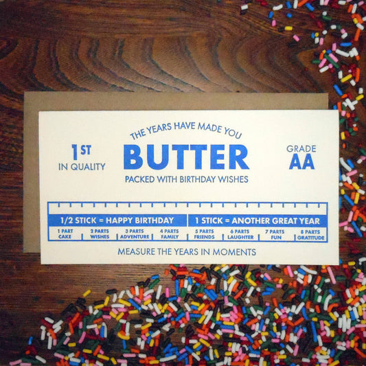 Card with text about butter and birthday wishes on a wooden surface with sprinkles.