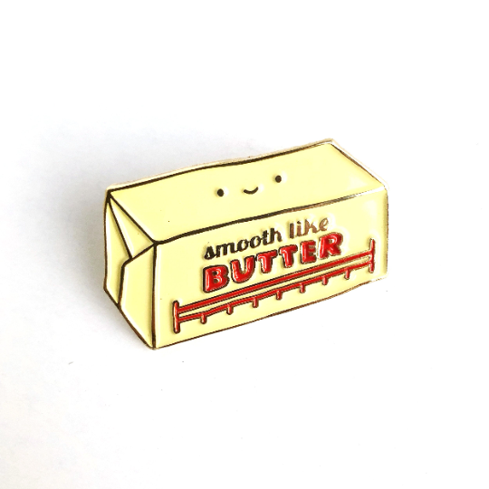 Butter enamel pin -- along with a face on it, it reads "Smooth like butter" 
