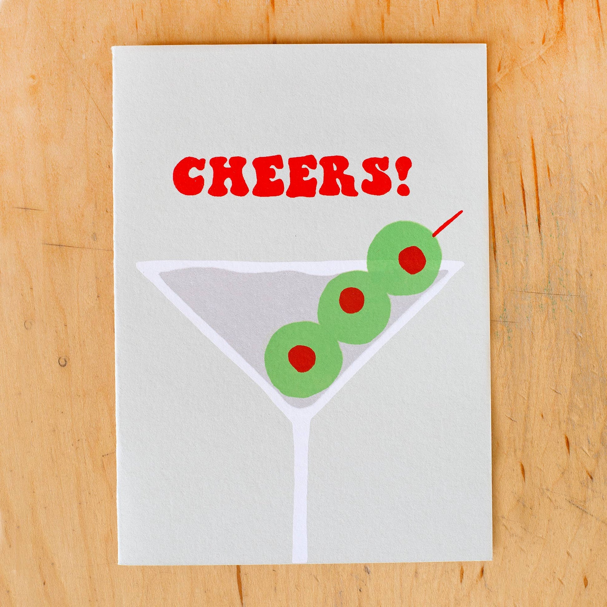 Greeting card that has martini glass with olives on it and reads "Cheers!" in bold red