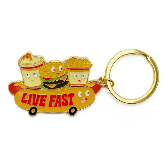 Enamel keychain with three characters shaped like a hamburger, soda, and box of french fries riding on a hot dog with wheels! Text on the hot dog reads "Live Fast"