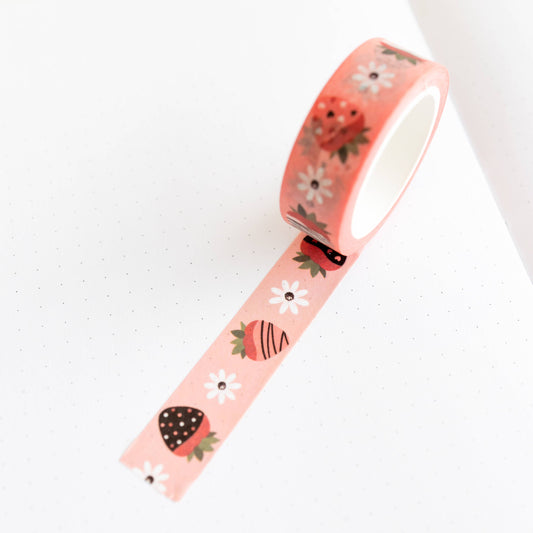 Roll of pink washi tape with different chocolate covered strawberries and white flowers on it 