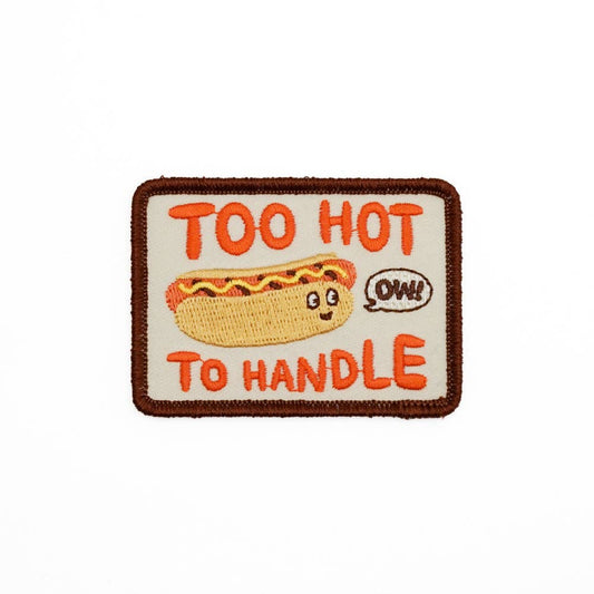 Rectangular embroidered patch -- Stitched brown border, orange text reads "Too hot to handle" with a hot dog in center and a thought bubble that reads "ow!" 