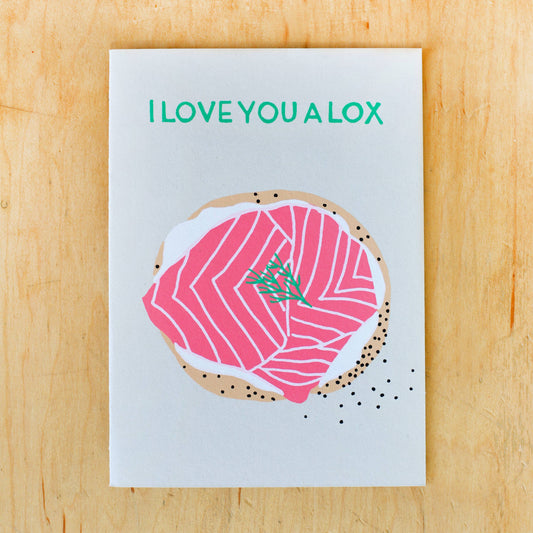 Greeting card that reads "I love you a lox" and has an image of an open faced bagel spread with cream cheese, lox and dill on it 