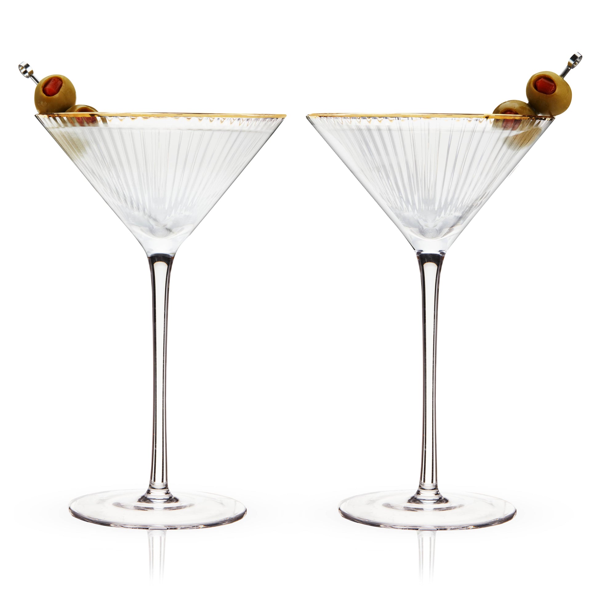Photo of two rippled crystal martini glasses with gold dipped rims. Portrayed with green martini olives speared on silver cocktail picks resting inside the glasses.. Background is white.