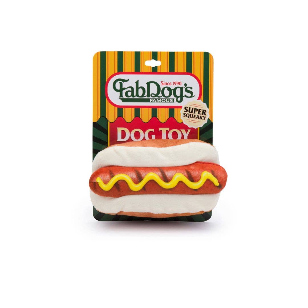 Dog toy that looks like a hot dog with grill marks and a single squiggle of mustard. Shown in green and yellow striped packaging.