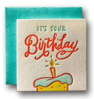 Tiny greeting card that reads "it's your birthday" with one candle on a cake