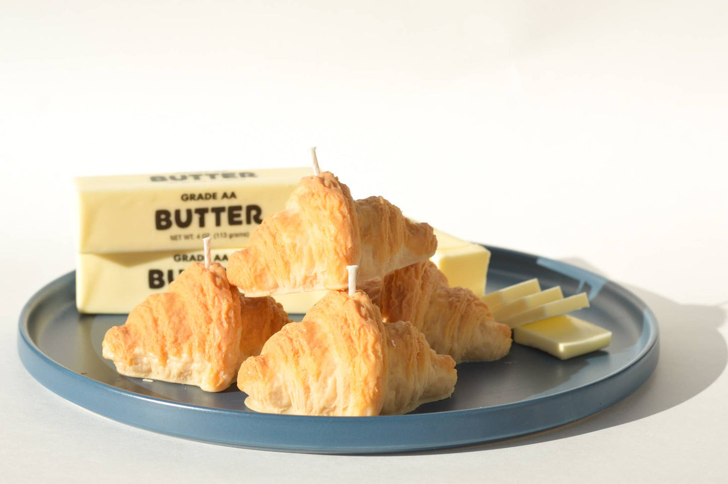Pile of four croissant candles on a plate next to slabs of butter.
