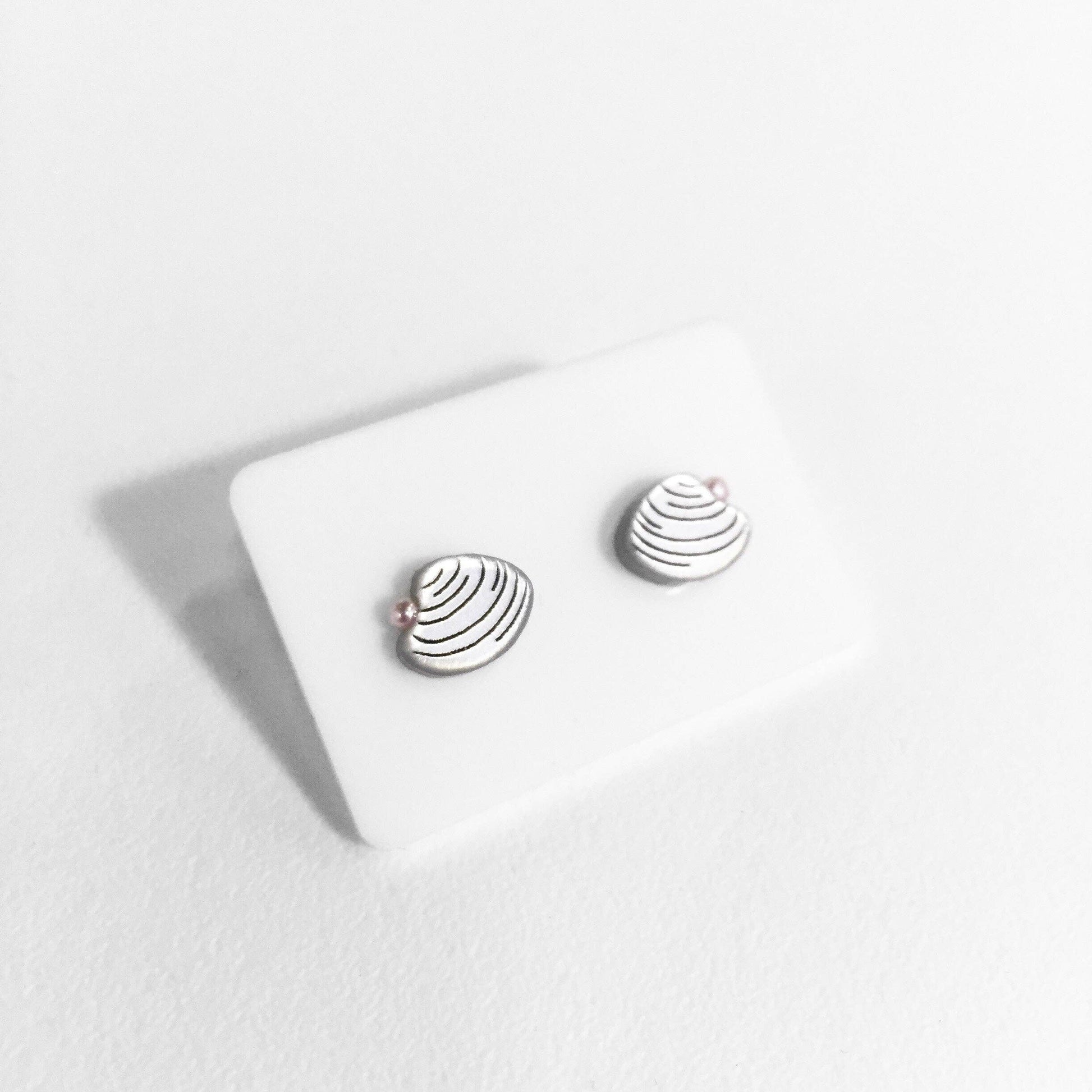 Close up of mini clam stud earrings in silver with card backing 