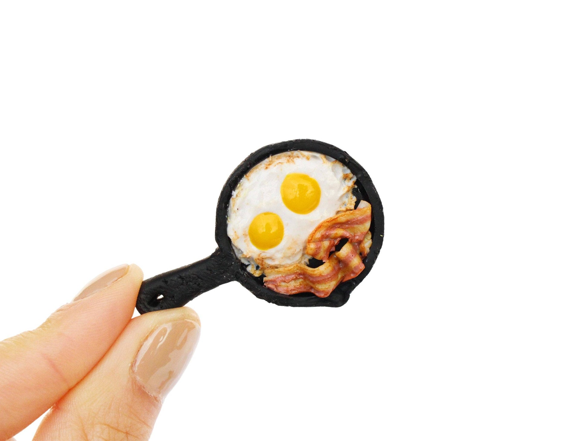 Tiny handmade magnet featuring bacon and 2 eggs in a skillet.
