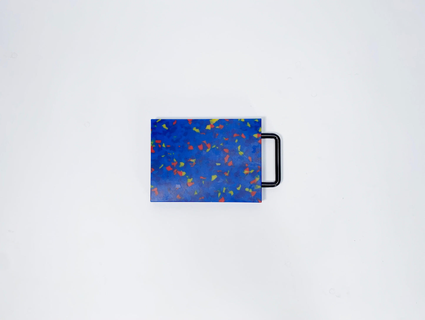 Small blue cutting board with yellow and red confetti and black handle 