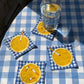 Set of 4 coasters photographed on top of a gingham blue tablecloth and a glass of water on one of them