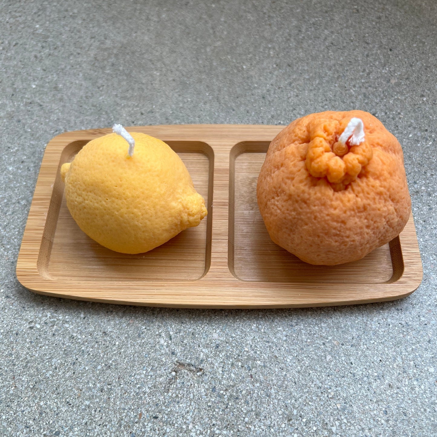 Wooden tray with two side by side, separate compartments. Each compartment is holding a candle, on the left a lemon and on the right, an orange. 