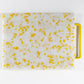 Mostly white cutting board with yellow confetti throughout, handle is yellow