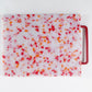 White cutting board with red and orange confetti throughout. Handle is red. 