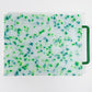 mostly white cutting board with blue and green confetti throughout, handle is green 