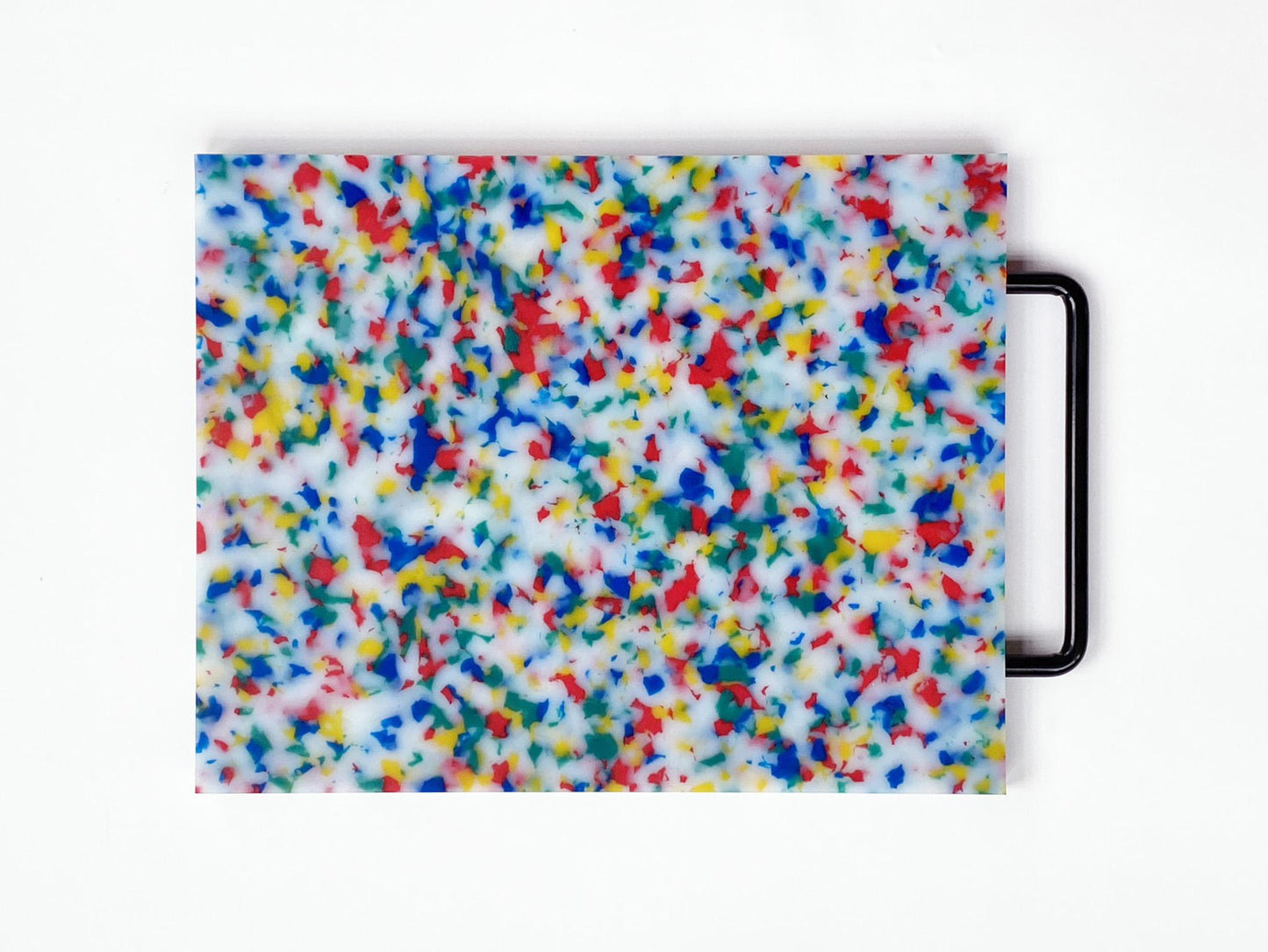 Cutting board in multi confetti -- red, yellow, blue and green confetti throughout the board. Handle is black. 