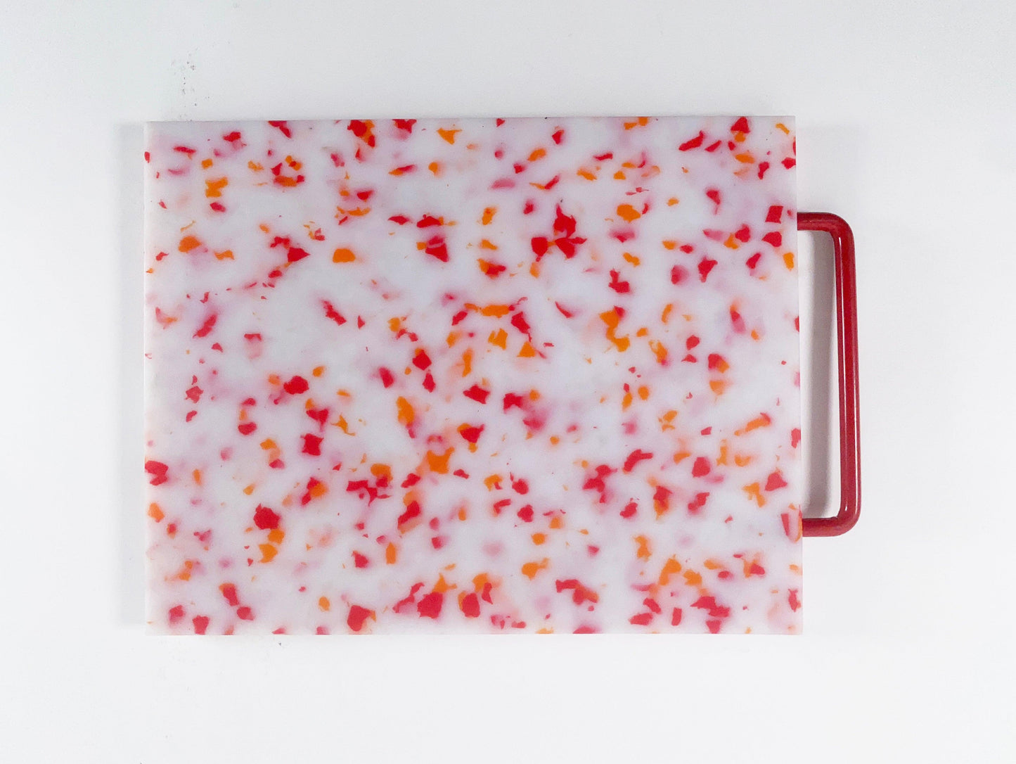 White cutting board with red and orange confetti throughout. Handle is red. 