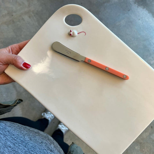 White, rectangular cheese plate with a loop and small mouse in the top left corner. Pink sabre on top of the plate. 