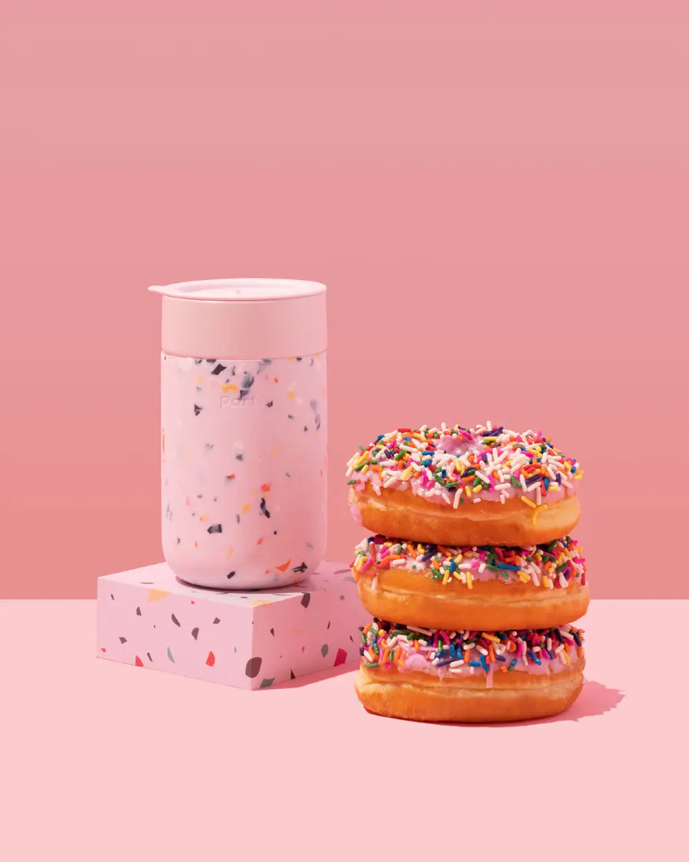 12oz to-go terrazzo tumbler in pink next to sprinkle donuts 